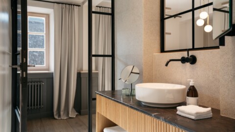 Modernes Badezimmer mit Waschtisch, Spiegel, Handtüchern und grossen Fenstern.