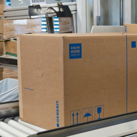 Braune Kartons mit dem Aufdruck "GEBERIT" auf einem Förderband in einem Lager.