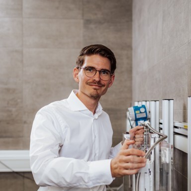 A man in a white shirt and glasses stands next to sanitary equipment.