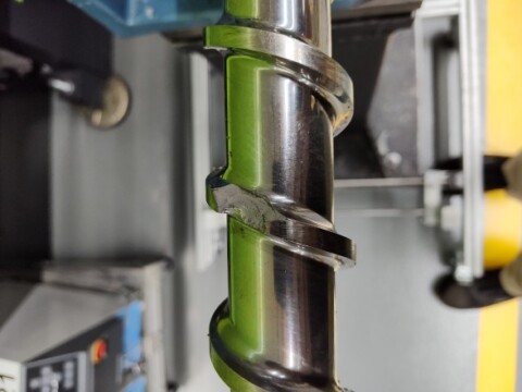 Close-up of a metallic drill bit with a spiral fluted design, set against a machinery backdrop.