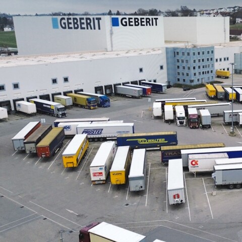 Aerial view of a logistics facility with numerous lorries parked in a loading area, surrounded by industrial buildings.