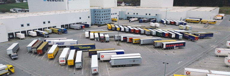 Aerial view of a logistics facility with numerous lorries parked in a loading area, surrounded by industrial buildings.