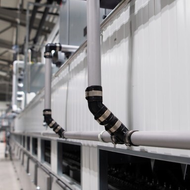 Gray pipes and fittings arranged along a white industrial wall in a spacious facility.