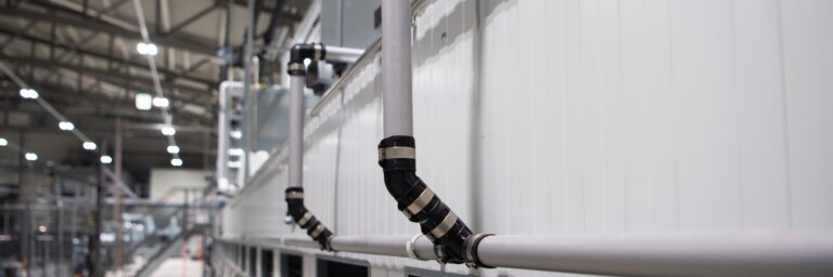 Industrial setting featuring pipes attached to a wall, with a blurred background of equipment and machinery.