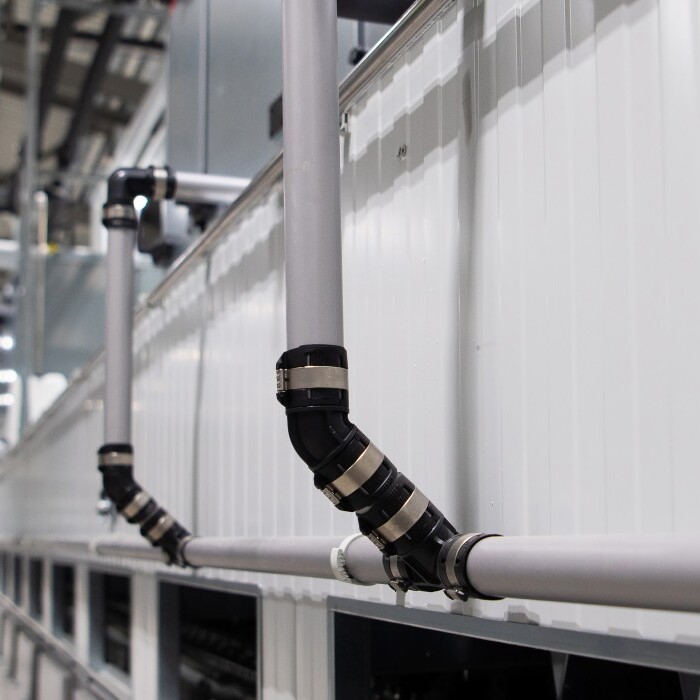 Industrial setting featuring pipes attached to a wall, with a blurred background of equipment and machinery.