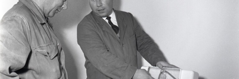 Two men look at a product, one demonstrating it while the other observes attentively.