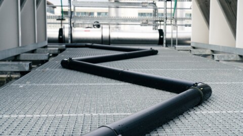 Schwarze Rohre, die auf einem gitterartigen Boden verlaufen und eine zickzackartige Anordnung bilden.