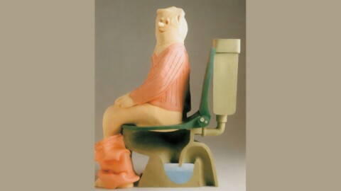 A sculpture wearing a pink sweater sitting on a toilet.