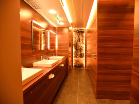 Modern restroom featuring brown wood paneling, sinks, wall mirrors, and a decorative partition.