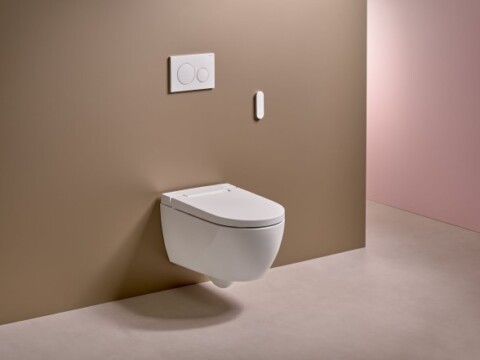 A modern, wall-mounted toilet with a flush panel on a brown wall and a light pink background.