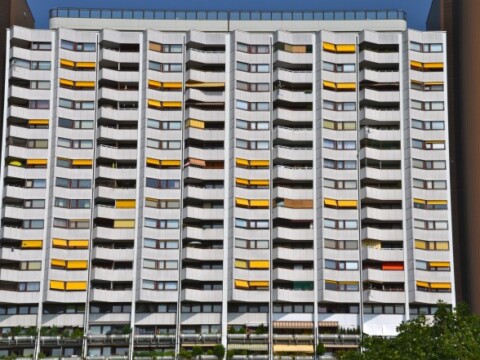 A tall residential building with numerous balconies, featuring yellow awnings and a modern design.