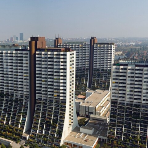 A panoramic view of multiple modern high-rise residential buildings with greenery in the foreground and a city skyline in the background.