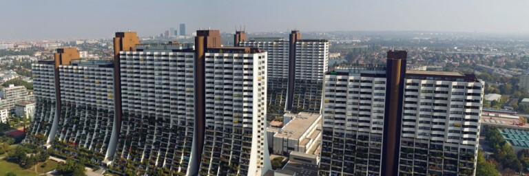 A panoramic view of multiple modern high-rise residential buildings with greenery in the foreground and a city skyline in the background.