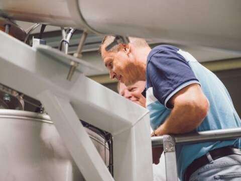 Zwei Personen, die interessiert in einen grossen Behälter schauen, während sie auf einer Plattform stehen.