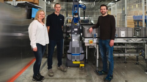 Drei Personen stehen in einem modernen Lagerhaus neben einem Roboter.