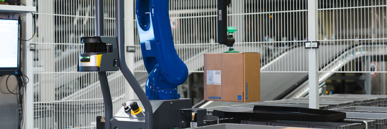 Industrieroboter hebt einen Karton in einem automatisierten Lager.