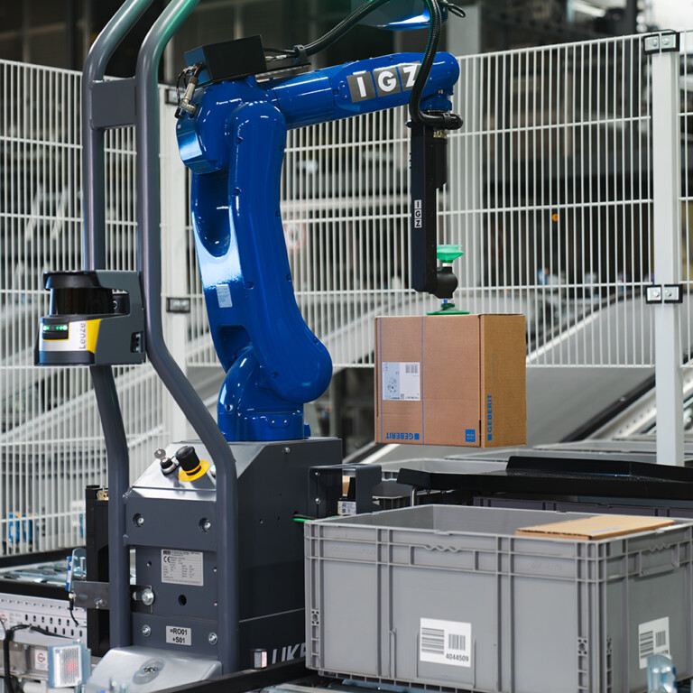 Industrieroboter hebt einen Karton in einem automatisierten Lager.