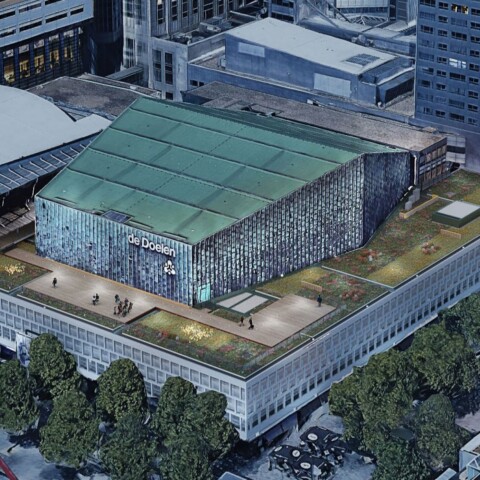 Aerial view of a large modern building with a green roof, surrounded by urban architecture and trees.