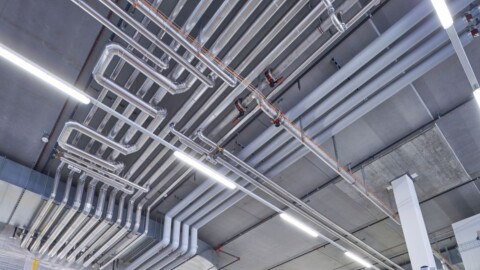 Überkopfansicht von Rohren und Leitungen an einer modernen Decke in einem Gebäude.