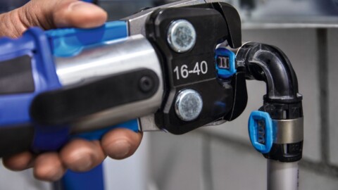 Eine Hand hält ein Werkzeug zum Verpressen von Rohrverbindungen.