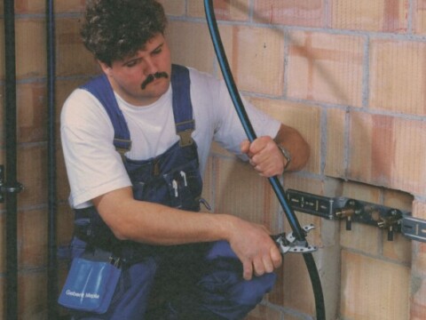Ein Handwerker installiert Rohre in einer Wand mit Ziegelsteinen.