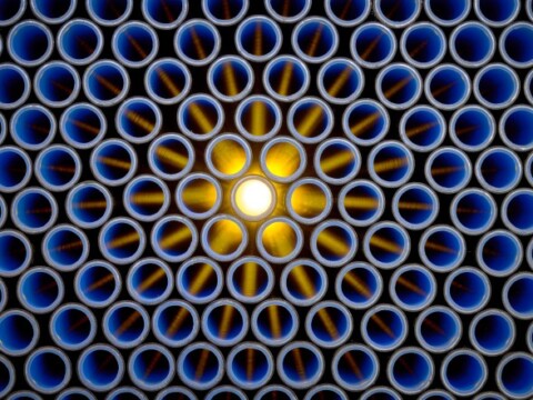 Ein symmetrisches Muster aus blauen Rohren, wobei in der Mitte ein leuchtendes, goldenes Licht strahlt.