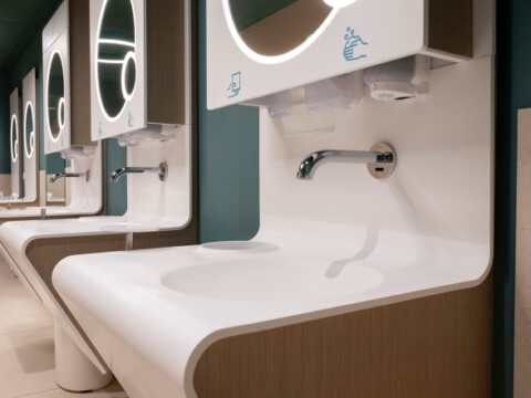 Modern restroom with several white sinks, mirrors, and soap dispensers, featuring a clean and minimalist design.