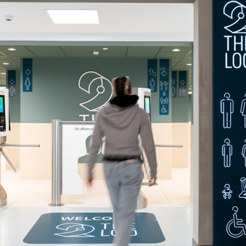 A person walks towards a restroom entrance, with directional signage on the walls indicating bathroom options and accessibility features.