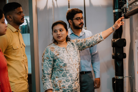 A group of four individuals stands around a display, with one person pointing to a pipe system.