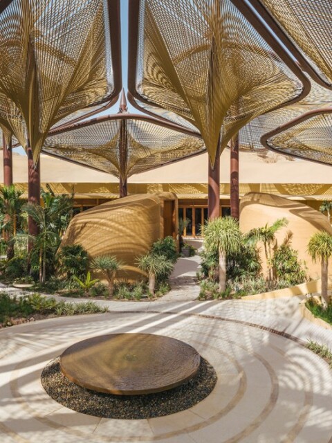 A spacious, modern outdoor area with large, artistic canopy structures and lush greenery surrounding.