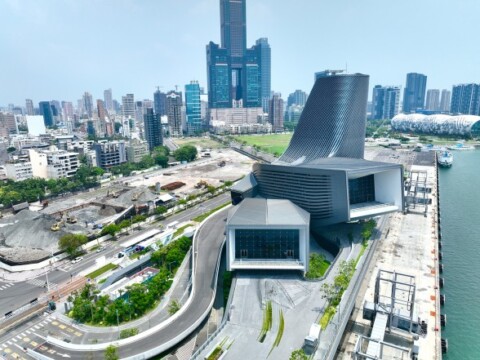 Aerial view of a modern architectural structure with flowing lines, surrounded by a cityscape and waterfront.