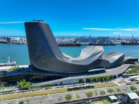 A modern architectural structure situated by a waterfront with a clear blue sky in the background.
