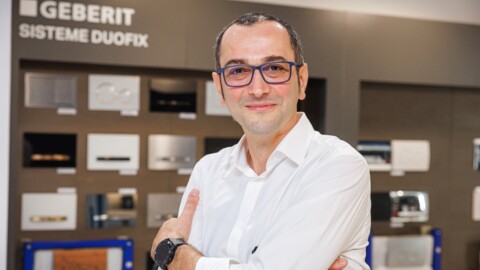 A man with glasses and a white shirt stands confidently, smiling, in front of a display featuring various bathroom fixtures.
