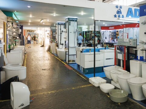 A display area of a home improvement store featuring various types of bathroom fixtures, including toilets and sinks, along a wide aisle.