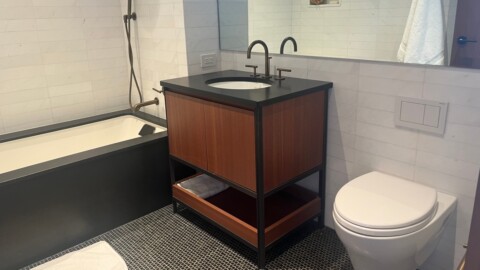 A modern bathroom featuring a wooden vanity with a sink, a bathtub, and a toilet, with a mirror and light tiles.