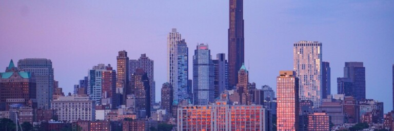 City skyline featuring a mix of modern skyscrapers during a sunset with pastel skies.