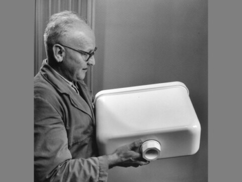 Ein Mann mit Brille hält einen weissen Spülkasten in der Hand.