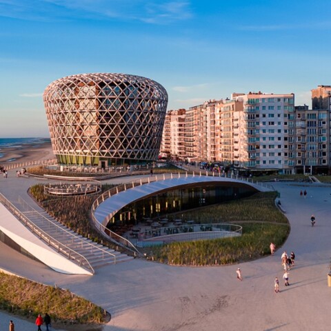 Coastal view featuring modern architecture with a distinctive round building, sandy beach, and residential structures along the shoreline.