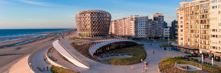 Coastal view featuring modern architecture with a distinctive round building, sandy beach, and residential structures along the shoreline.