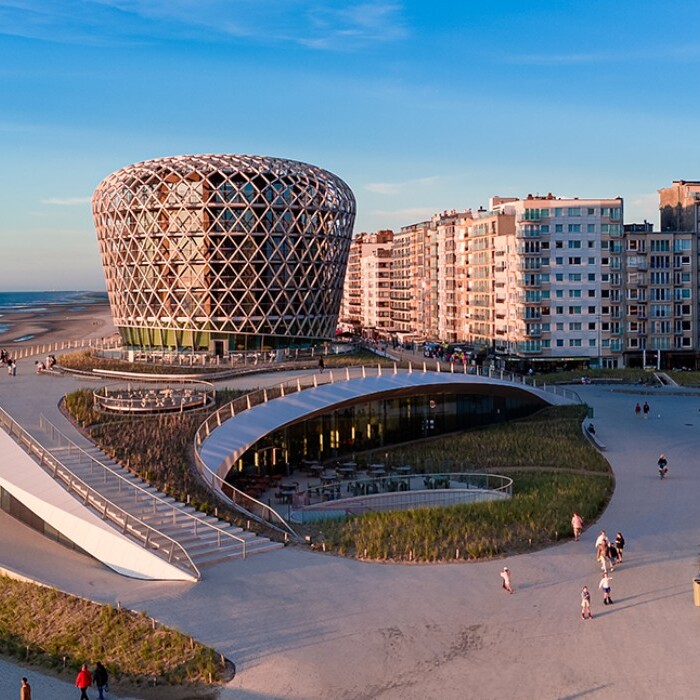 Coastal view featuring modern architecture with a distinctive round building, sandy beach, and residential structures along the shoreline.
