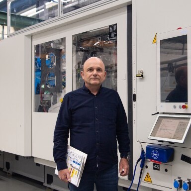 Ein Mann steht neben einer grossen, modernen Maschine in einer Fabrikhalle.