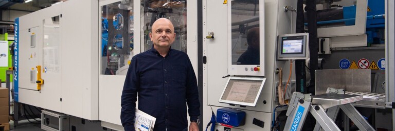 Ein Mann steht in einer Fabrikhalle neben einer grossen, modernen Maschinenanlage.