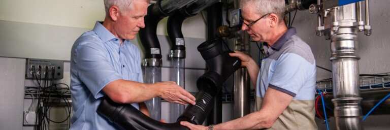 Zwei Männer in einem technischen Raum untersuchen ein grosses Rohrstück, während sie es miteinander vergleichen.