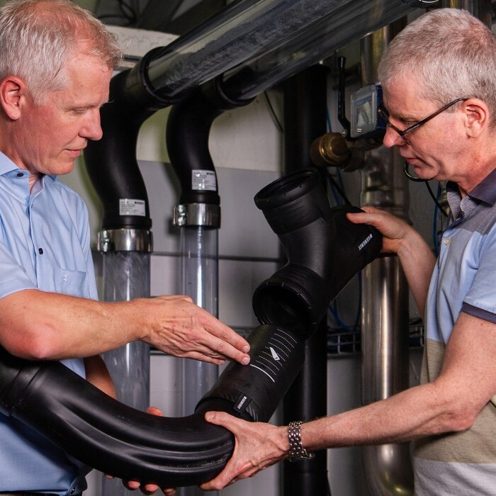 Zwei Männer in einem technischen Raum untersuchen ein grosses Rohrstück, während sie es miteinander vergleichen.