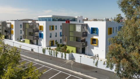 A modern apartment complex featuring colourful window frames and balconies, surrounded by trees and a parking lot.