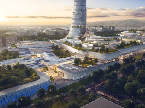 Aerial view of a modern urban complex featuring futuristic buildings, green spaces, and solar panels under a sunset sky.