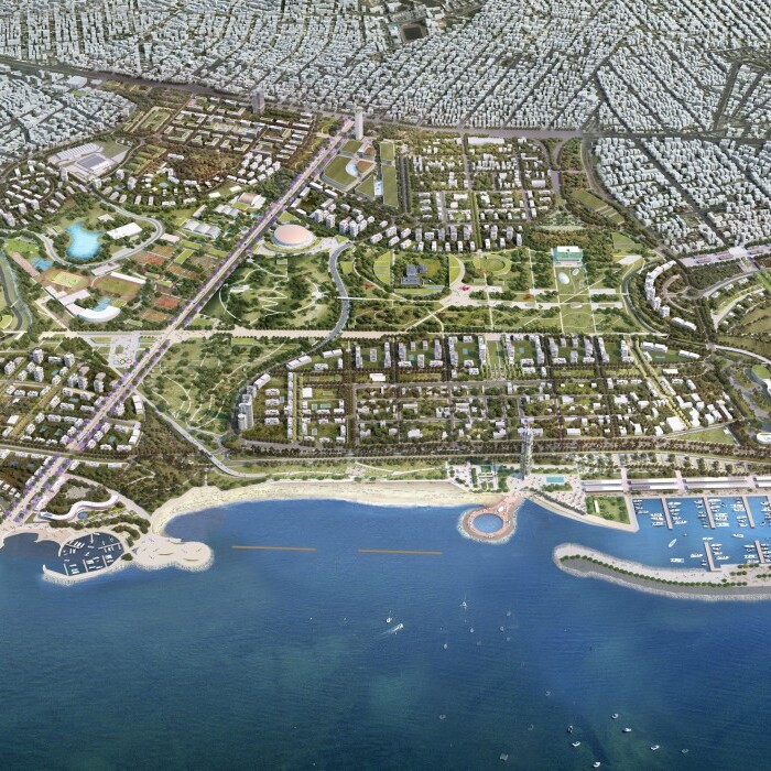 Aerial view of a coastal urban development featuring green spaces, residential areas, and a marina along the shoreline.