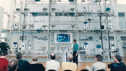 Eine Präsentation mit einem Referenten vor einer grossen, technischen Installation und einer Gruppe von Zuhörern.