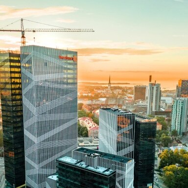 Moderne Wolkenkratzer und Gebäude in einer Stadtlandschaft bei Sonnenuntergang, umgeben von Bäumen und Strassen.