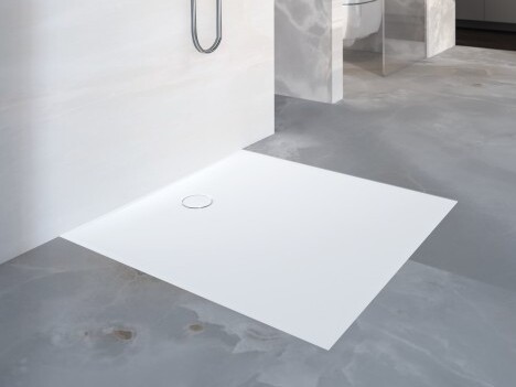 A minimalist shower floor made of white material, featuring a circular drain.